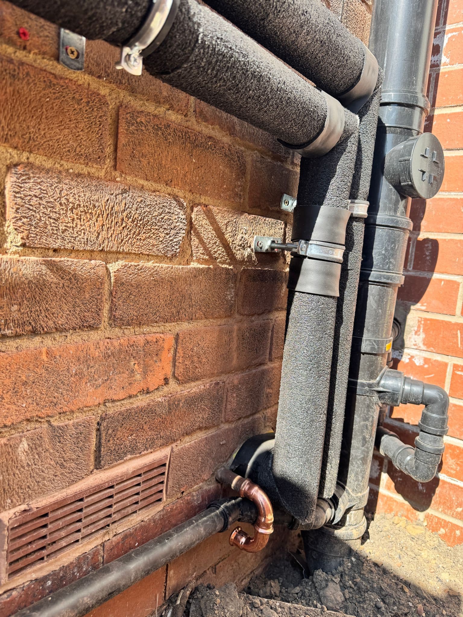 Heat pump flow and return pipework lagged and weatherproofed against an external brick wall